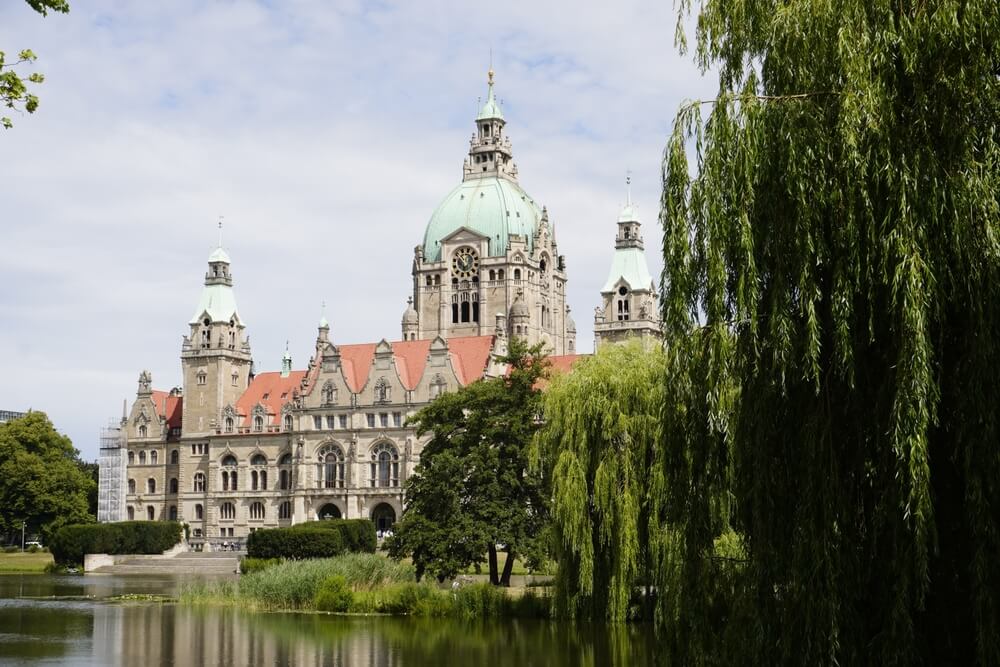 Luftbild von Hannover mit der markanten roten Rathauskuppel, umgeben von grünen Parks und modernen Gebäuden